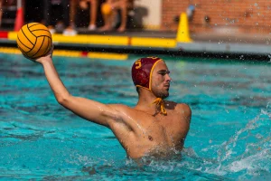 Alt Text: "USC water polo player in action, poised to throw a ball, wearing a cap with the number 5, showcasing skill and focus in a dynamic aquatic environment."